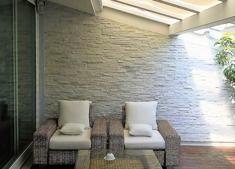 Terrasse mit Loungesesseln, dahinter Naturstein-Wandverblender in Beige