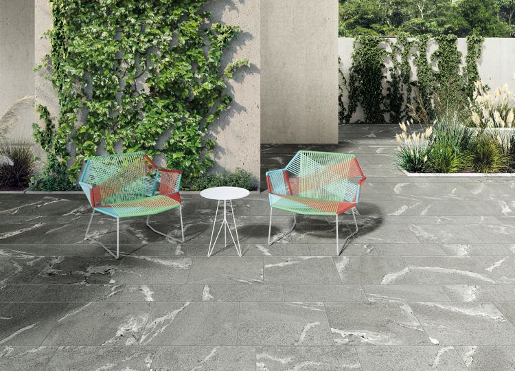 Terrasse mit großformatigen, grauen Steinoptikfliesen, zwei bunt bespannte Kunststoffsesseln und ein weißer kleiner Beistelltisch