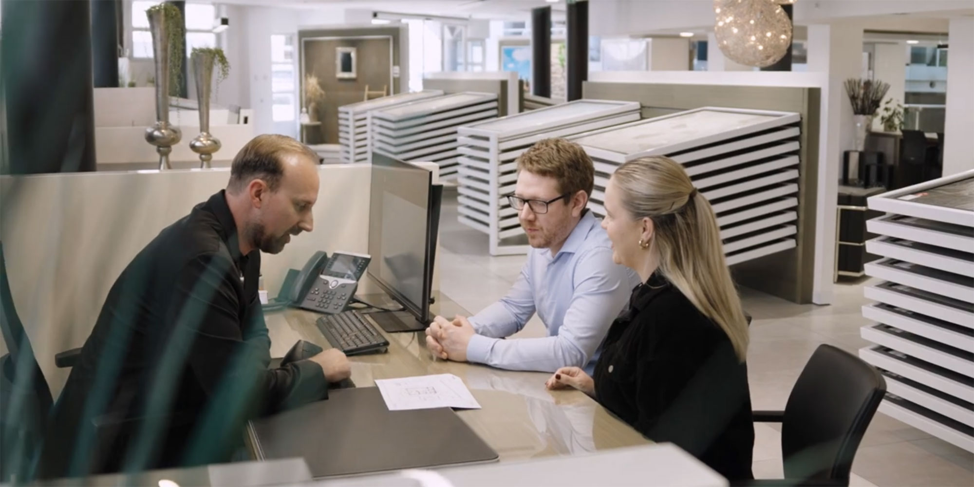 Ein Fliesenbachberater sieht sich mit 2 Kund:innen einen Plan an