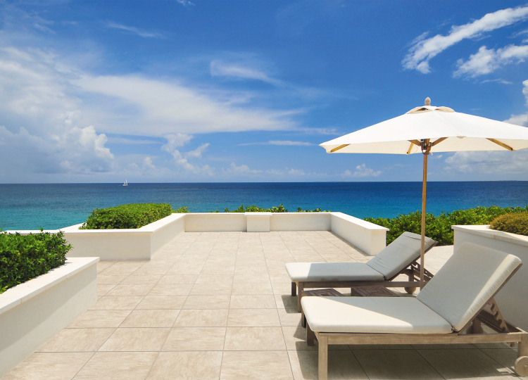 Urlaubsfeeling mit blick auf Meer und warmen Steinoptik Fliesen auf der Terrasse mit Liegestühlen und Sonnenschirm